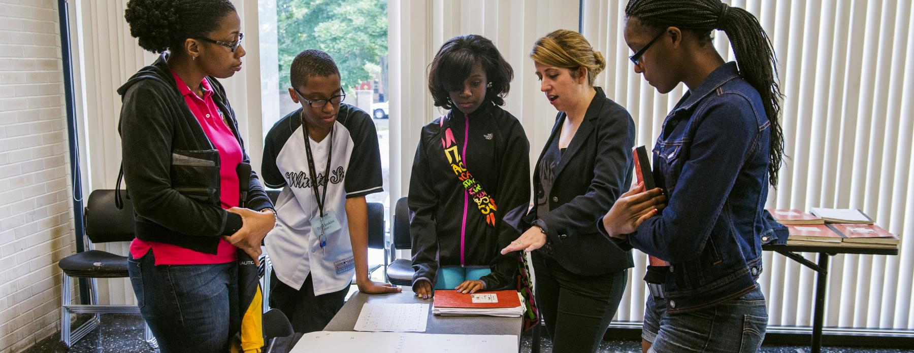 Students gather around a table with their teacher in class